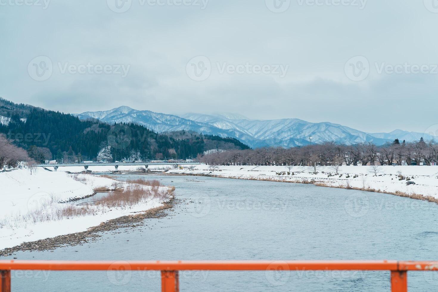 Hinokinai River riverbank with Yokomachi Bridge in winter season. Beautiful sakura trees flowers with snow and mountains locate in Kakunodate town, Semboku District, Akita Prefecture, Japan photo