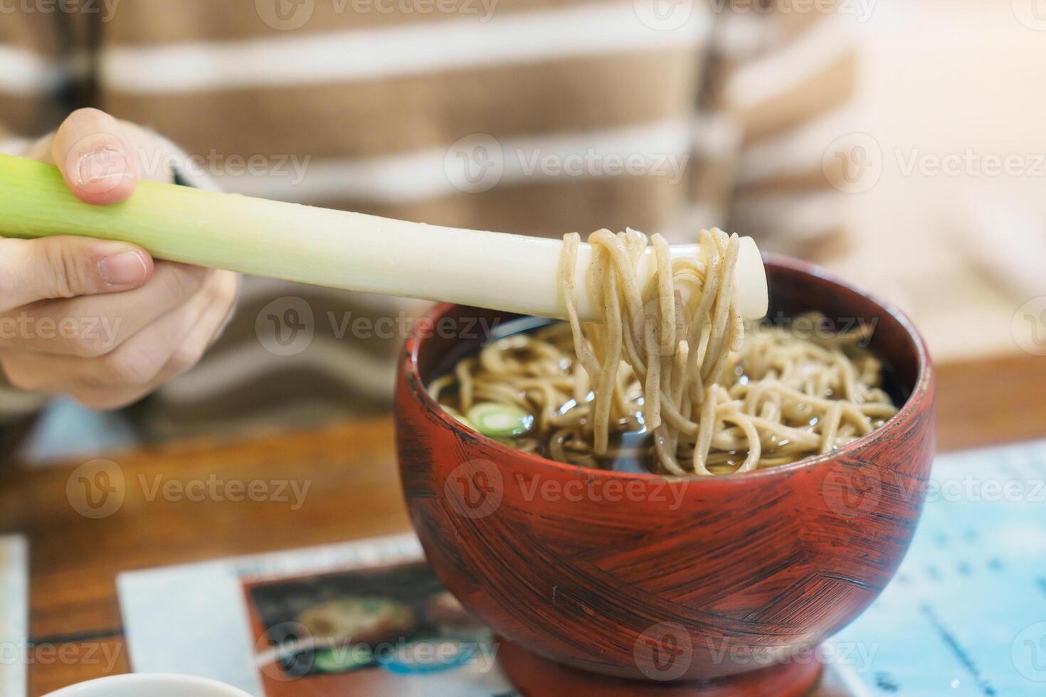 Woman tourist eating Negi Soba or Buckwheat noodles with a raw leek instead of chopsticks, famous soba when visit Ouchi Juku ancient farmer house in Shimogo, Minamiaizu, Fukushima Prefecture, Japan photo