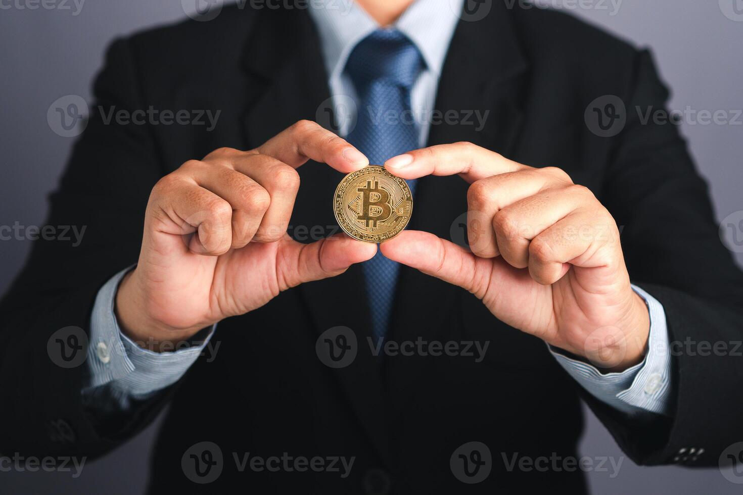 Hand of businessman showing a bitcoin golden coin while standing with a gray background. Close-up photo. Space for text. Virtual cryptocurrency and future money concept photo