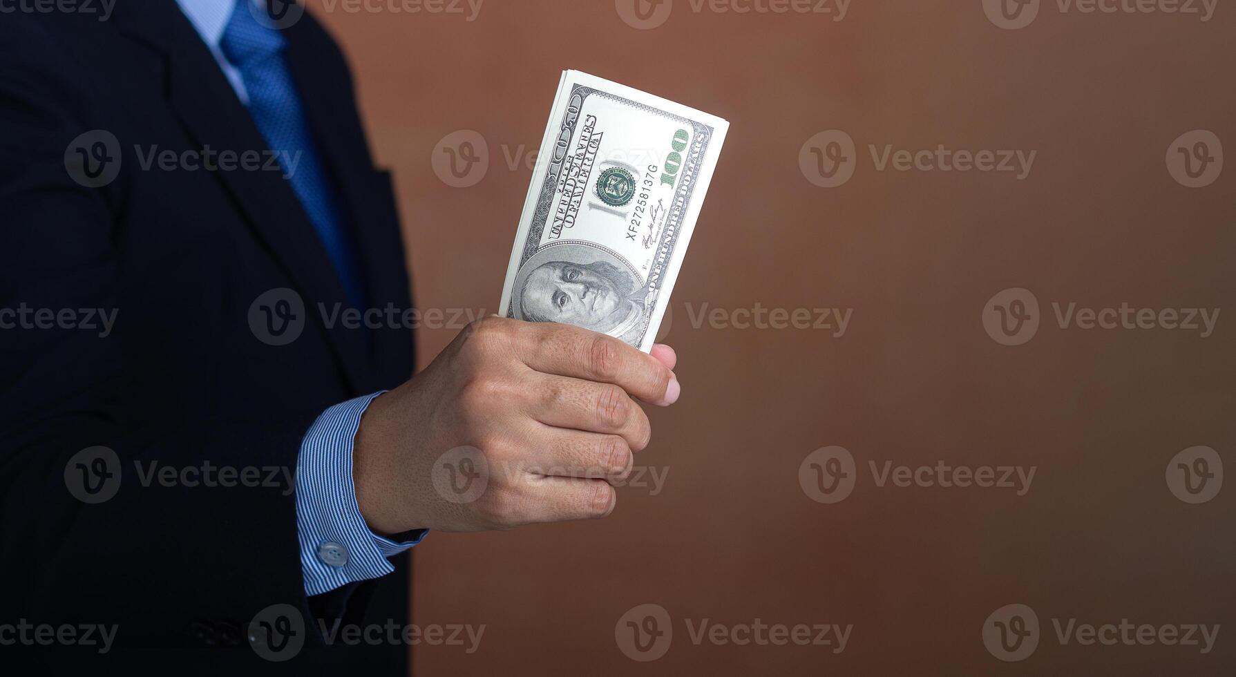Hand of a businessman holding US dollars while standing with a brown background. Personal loans or business loans. Space for text. Close-up photo. Business and finance concept photo