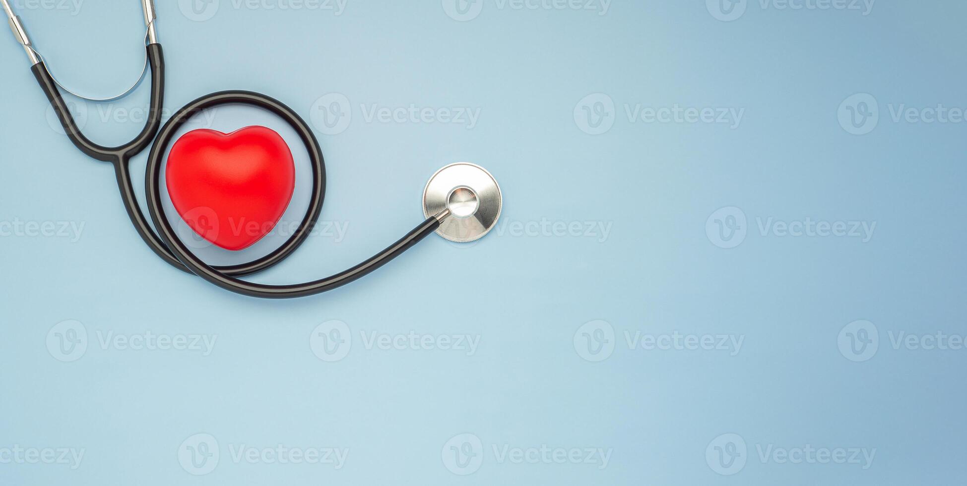 A stethoscope and red heart laid on a light blue background. Close-up photo. Top view. Flat lay. Space for text. Healthcare and medicine concept photo
