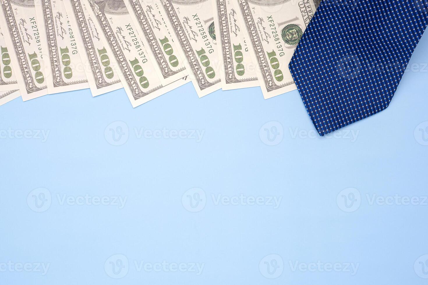 The top view of a blue tie laid on one hundred dollar banknotes isolated on a light blue background. Flat lay. Space for text. Happy Father's Day. Business and finance concept photo