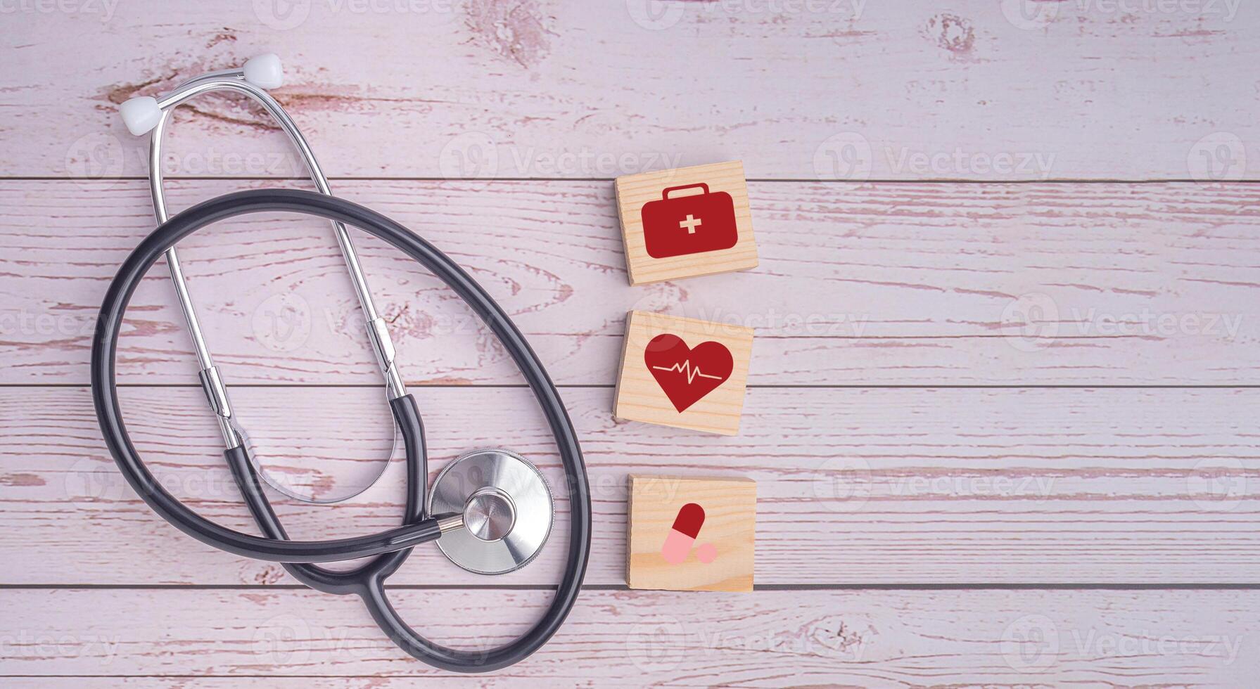 A stethoscope and wooden blocks with icons of health laid on wooden table. Close-up photo. Top view. Flat lay with Space for text. Healthcare and medicine with media icons concept photo