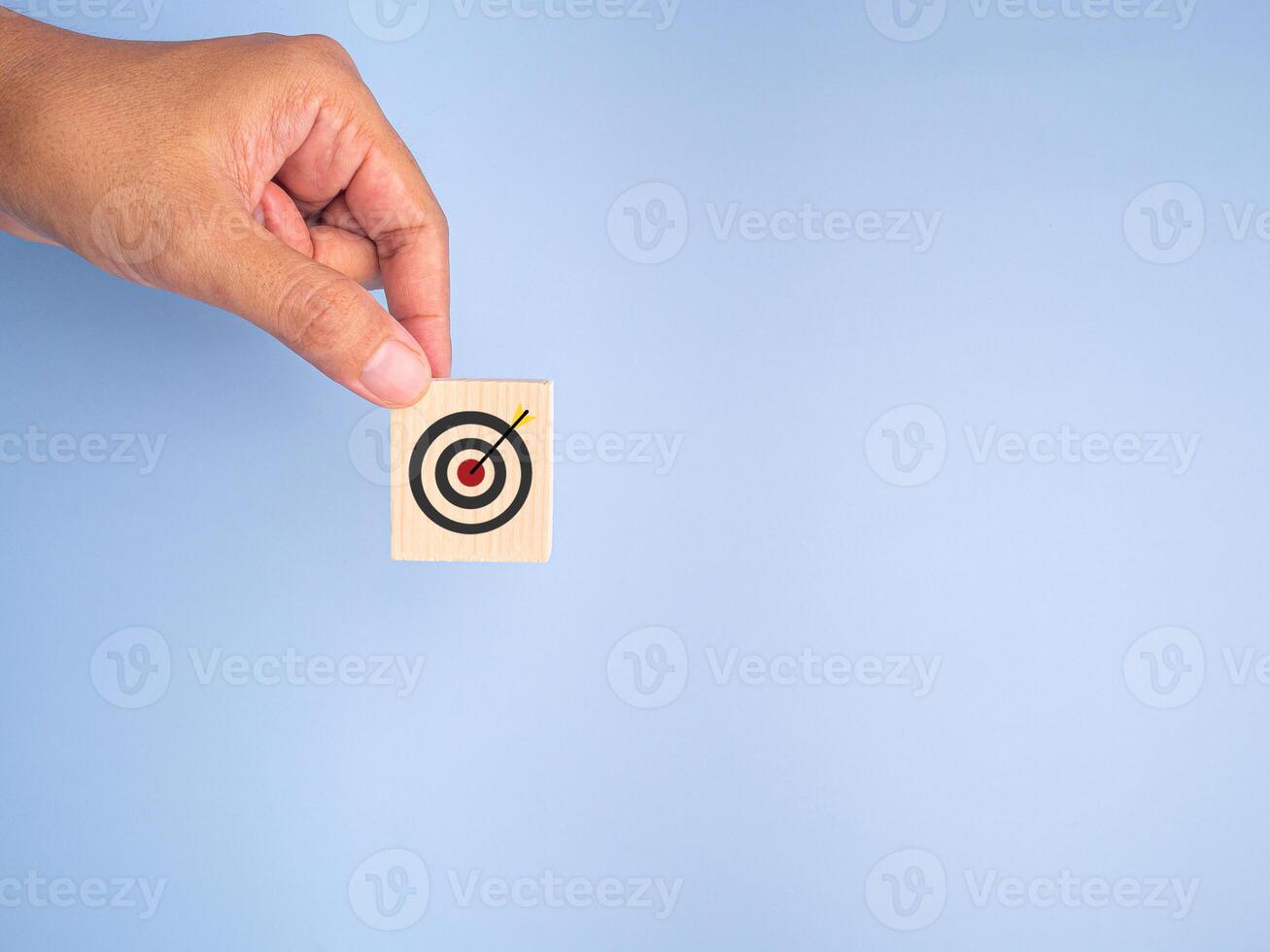 Hand holding of a wooden block with the goal icon isolated on a light blue background. Space for text. Business and strategy planning concept photo