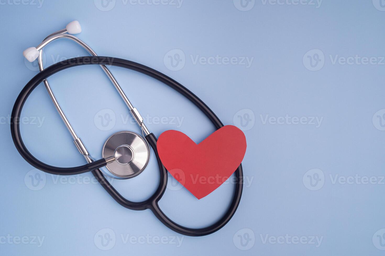 A stethoscope and red paper a heart shape isolated on a light blue background. Close-up photo. Top view. Flat lay with Space for text. Healthcare and medicine concept photo