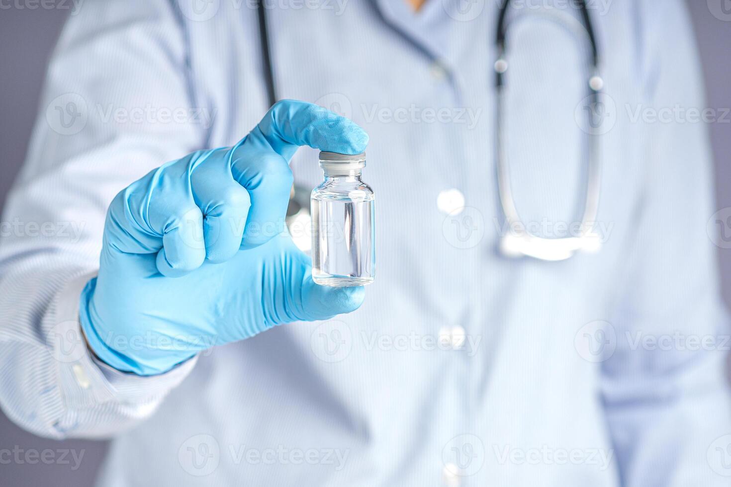 Doctor showing a vaccine bottle while standing with a gray background. Vaccine for immunization, and treatment from virus infection. Concept of medical and the fight against the virus photo
