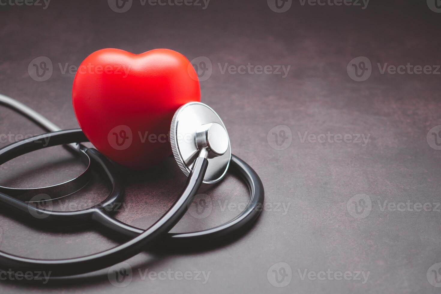 A stethoscope and red heart laid on vintage background. Close-up photo. Side view. Space for text. Healthcare and medicine concept photo
