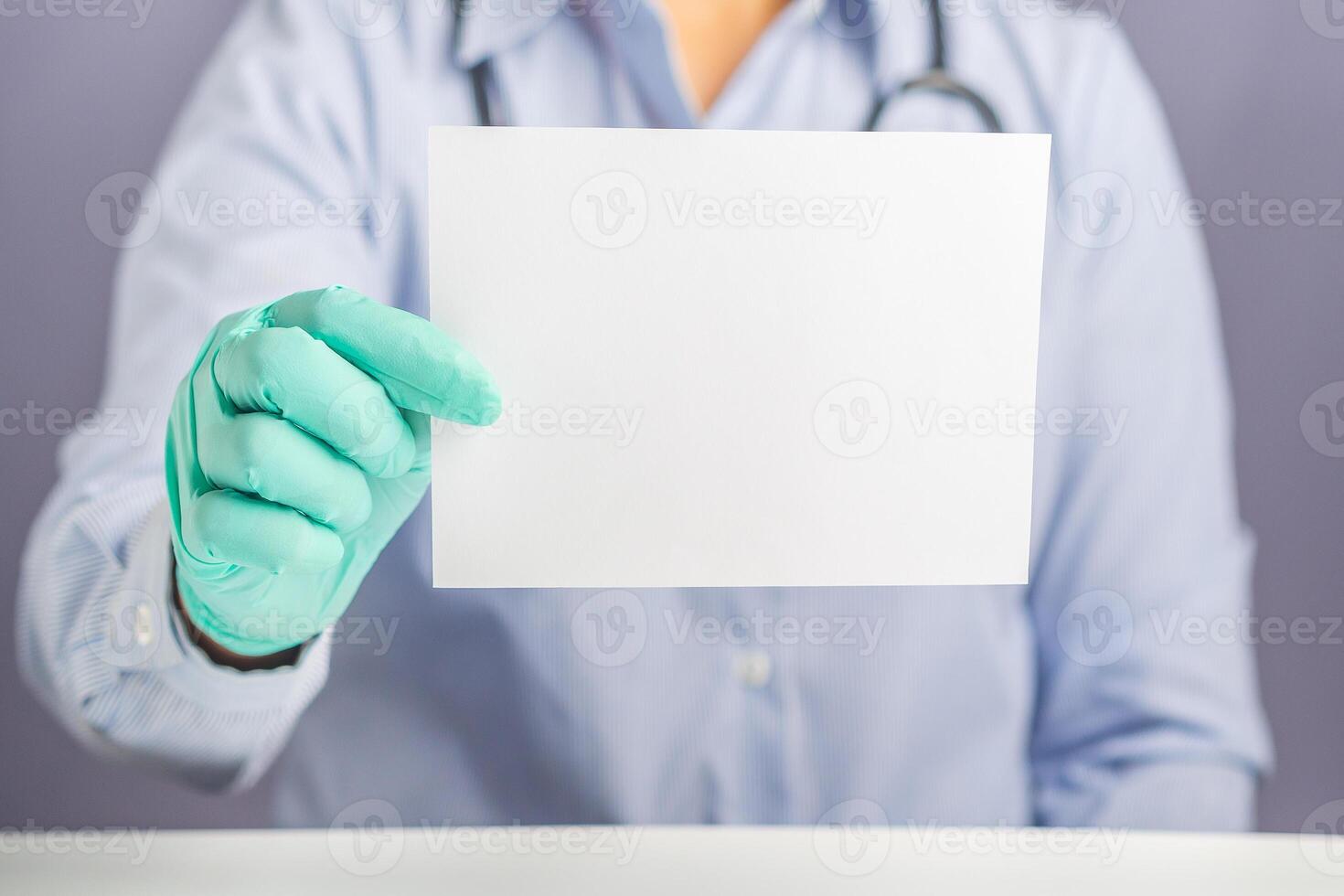 Hand of a doctor holding a blank white paper while sitting on a chair with gray background in the hospital or clinic. Close-up photo. Space for text. Medical and encouragement concept photo