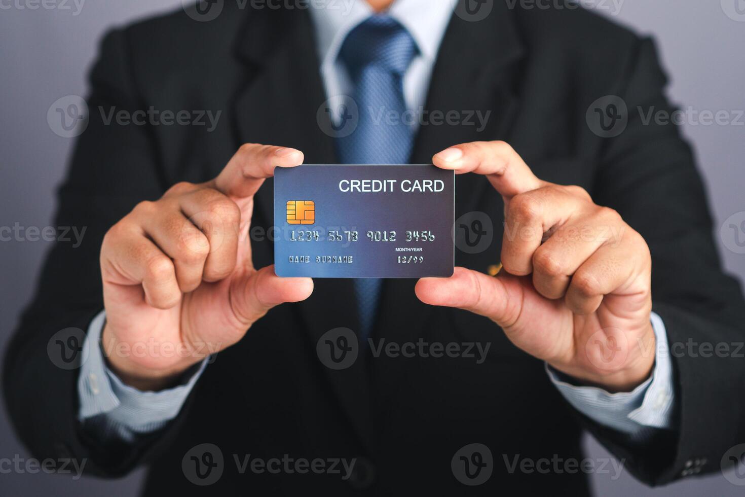 Businessman holding a mockup blue credit card while standing in a studio with copy space for text. Close-up photo. Money and business concept photo
