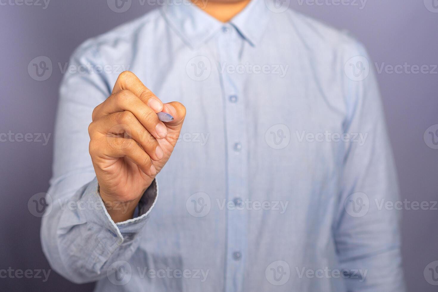 A businesswoman wearing a light blue shirt is holding a pen write or writing on the virtual screen or in the air against a gray background. Space for text. Modern business background concept photo