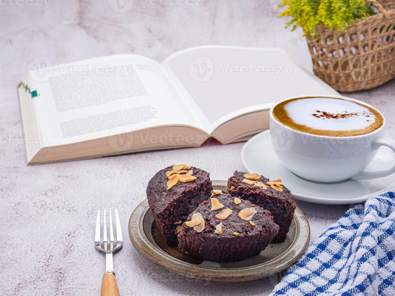 Pieces of fresh brownies on a plate with a book and a white coffee cup. Side view. Delicious chocolate pie. Dessert, beverage, and relaxation concept photo