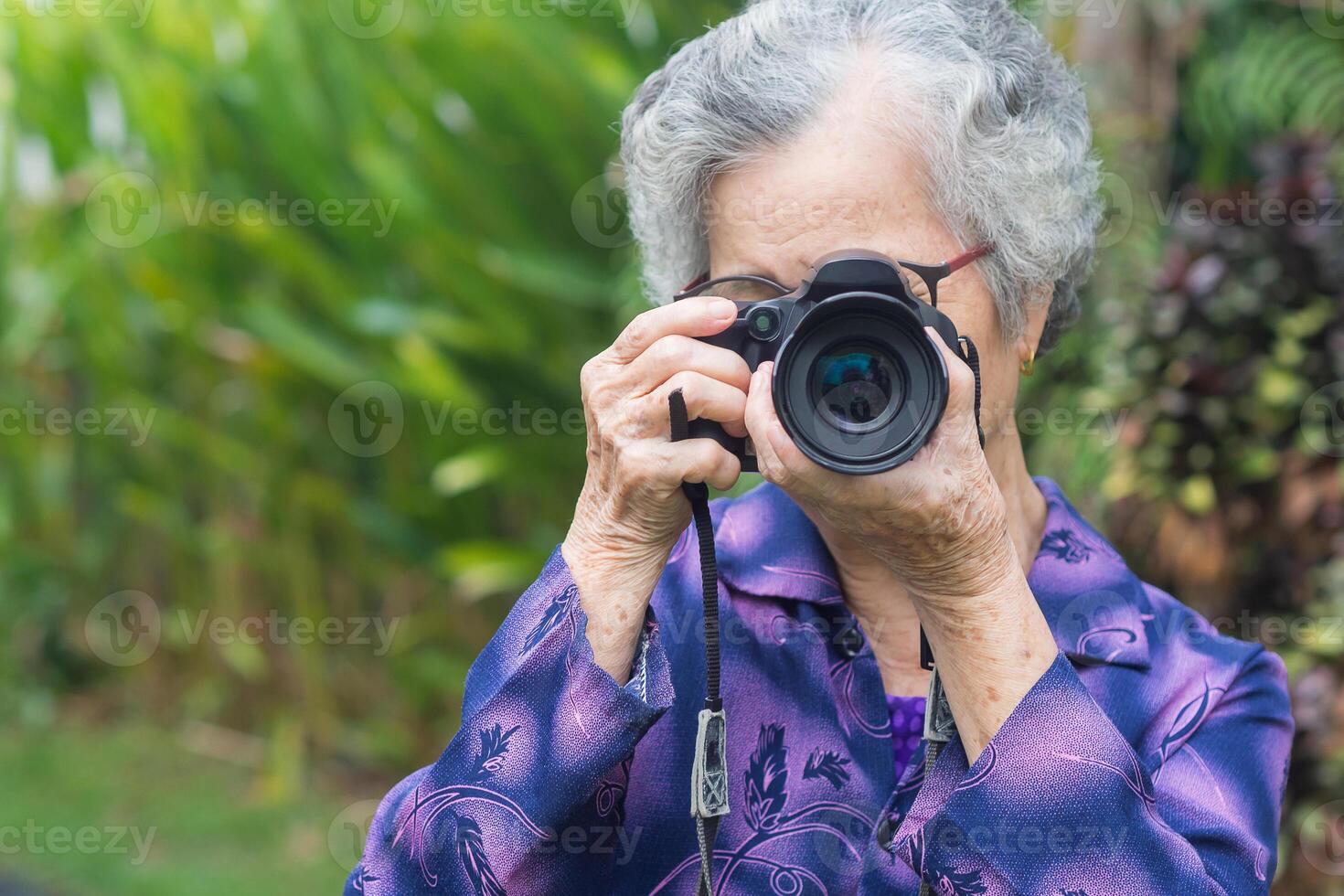 Happy senior woman taking photographs with a digital camera while standing outdoors. Aged people photographer and relaxation concept photo