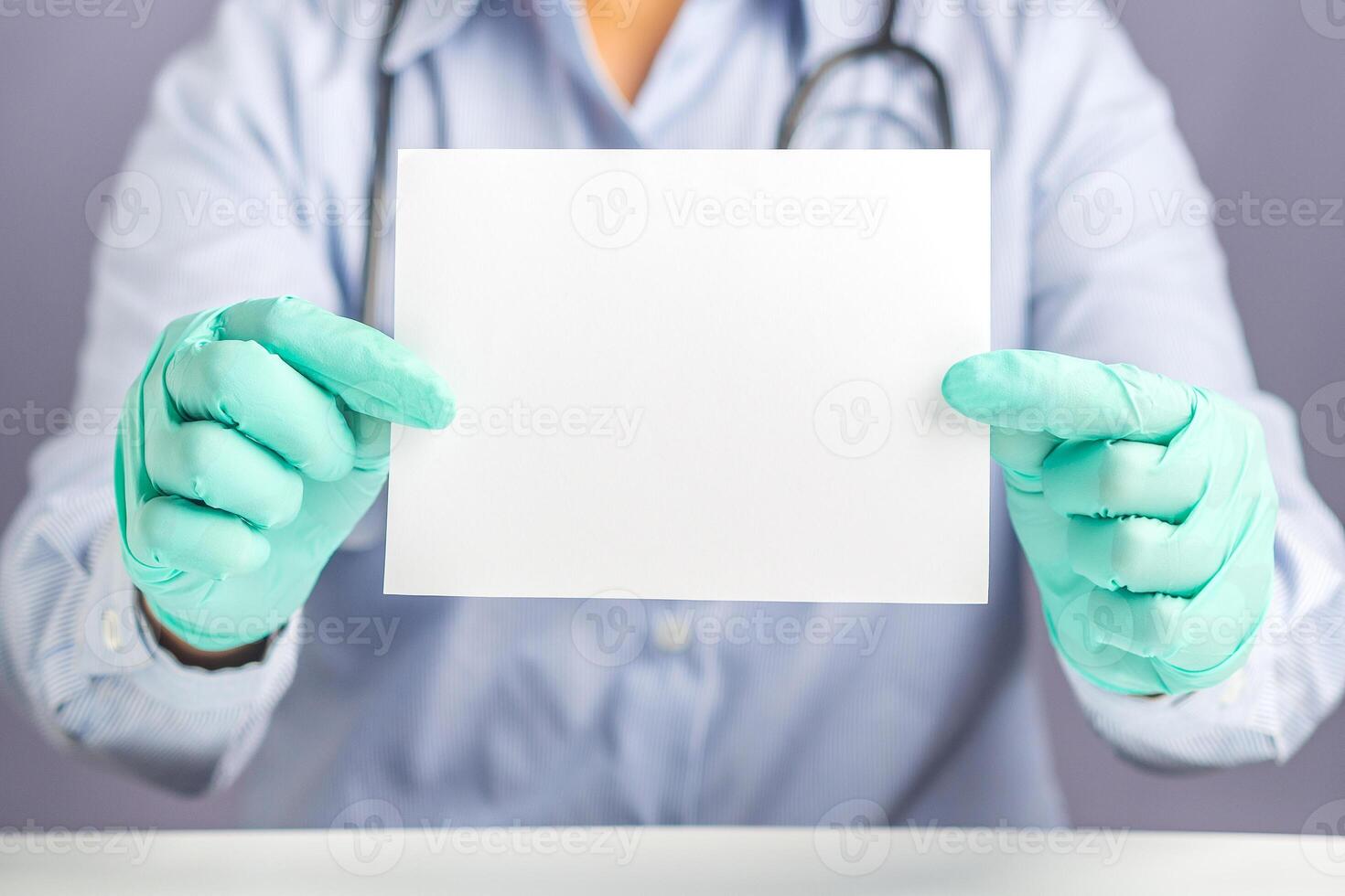 Close-up of doctor hands holding a blank white paper while sitting on a chair with gray background in the hospital or clinic. Space for text. Medical concept photo