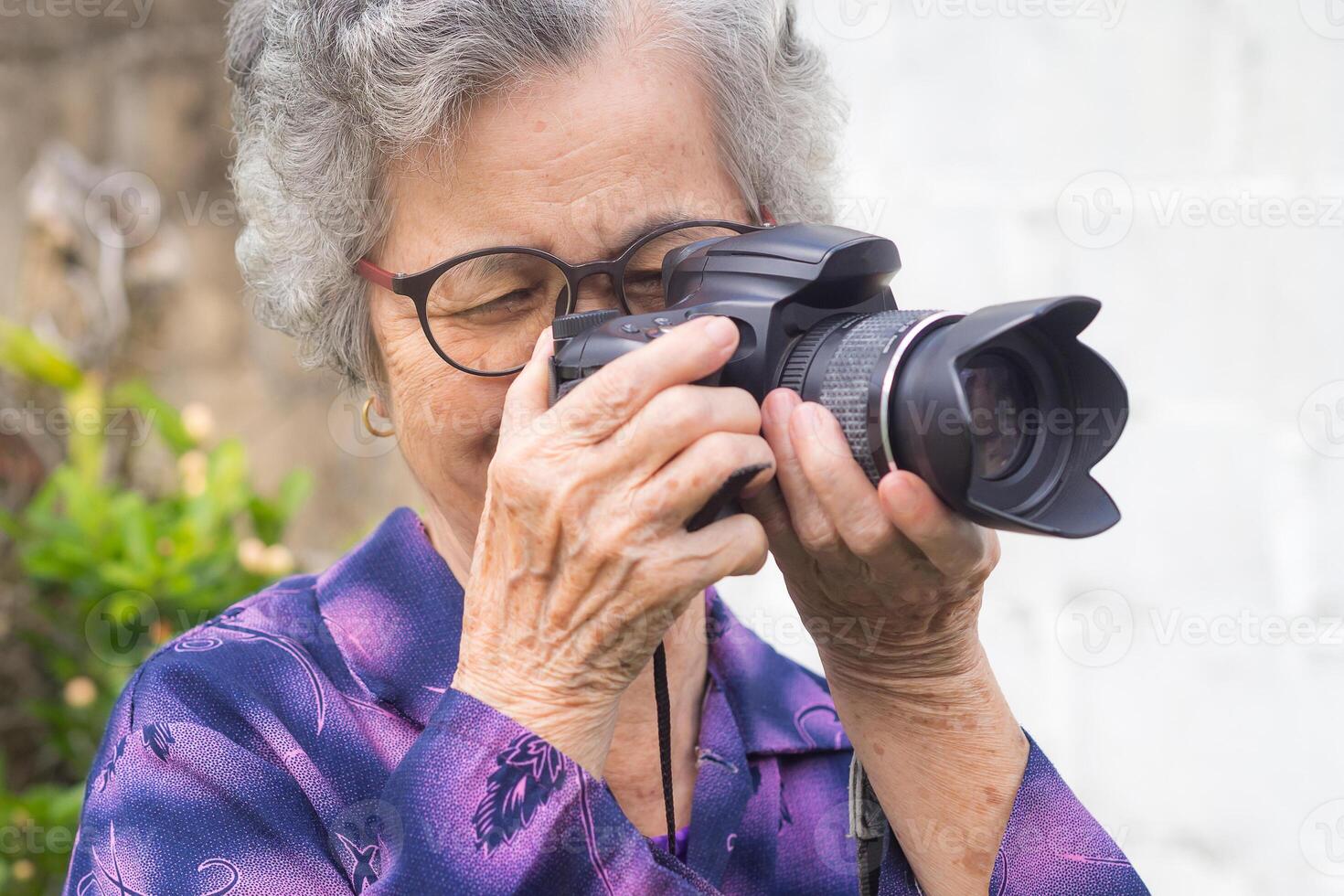 Happy senior woman taking photographs with a digital camera while standing outdoors. Aged people photographer and relaxation concept photo