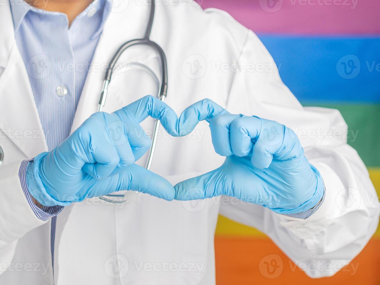 Doctor wearing gloves hands showing heart shape against the rainbow flag background. Medical help prophylaxis. photo