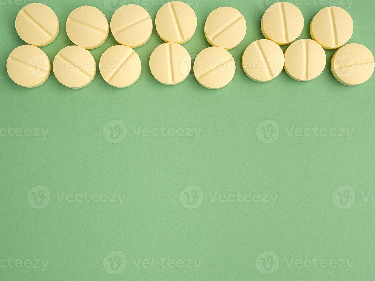 Pile of light yellow tablets medicine for people's health to heal diseases isolated on a green background. Space for text. Top view. Healthcare and medical concept photo