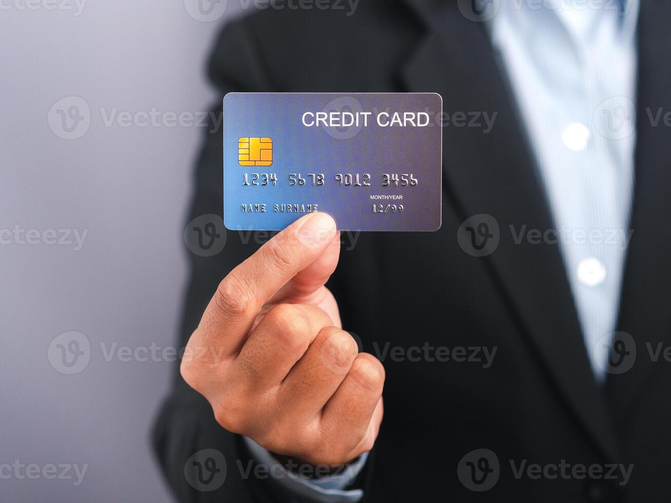 Businessman holding a mockup blue credit card while standing in a studio with copy space for text. Close-up photo. Money and business concept photo