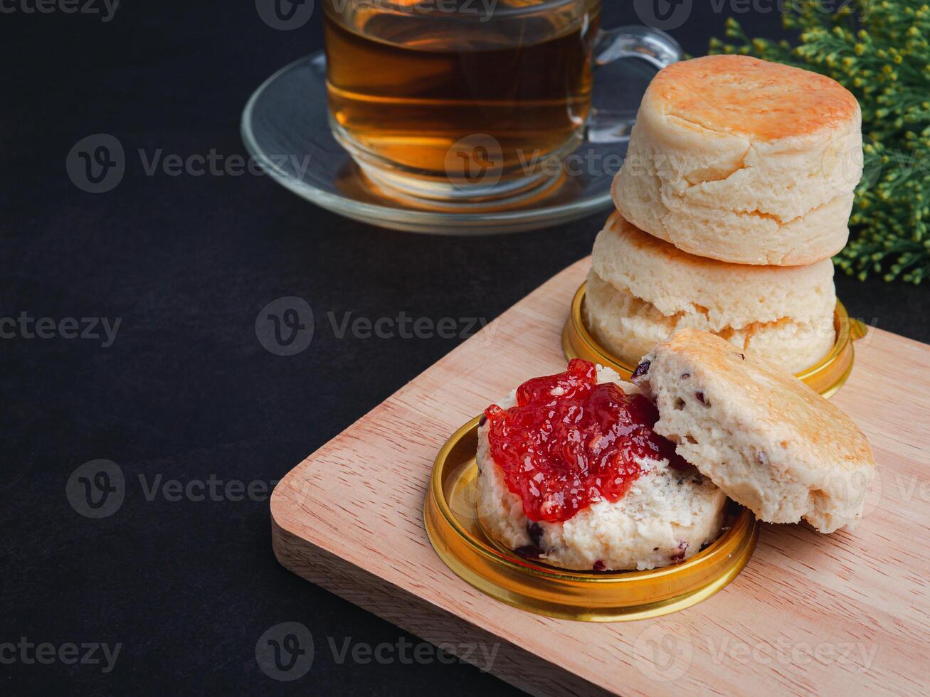 Traditional English style scones delicious freshly baked homemade with strawberry jam on a wooden cutting board and teacup on a dark stone background. Space for text. Dessert and beverage concept photo