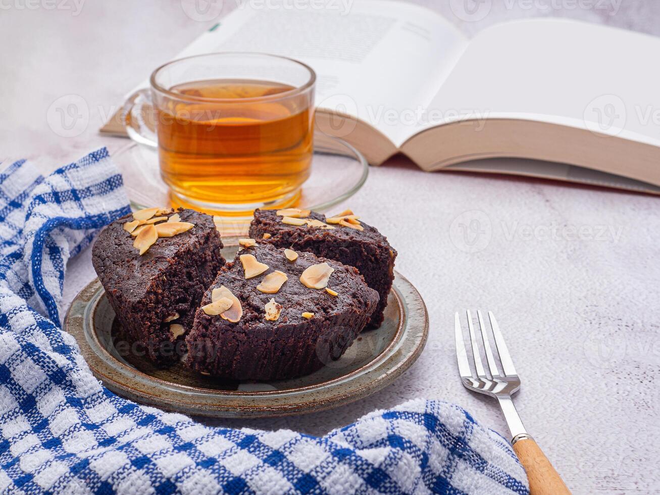 Pieces of fresh brownies on a plate with a book and teacup. Side view. Delicious chocolate pie. Dessert and relaxation concept photo
