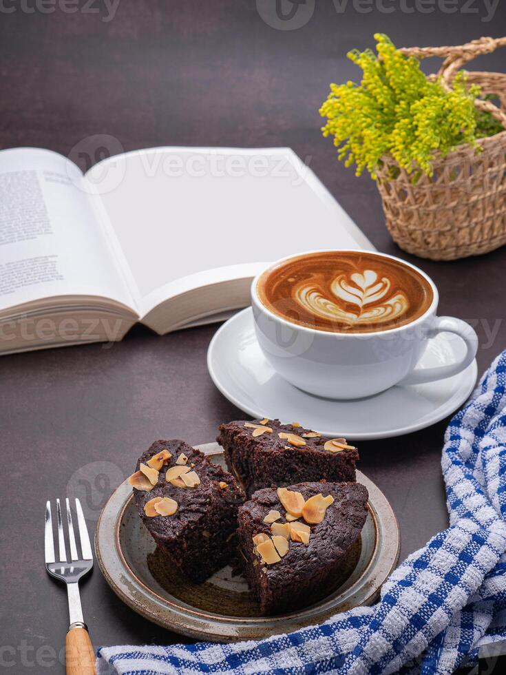 Pieces of fresh brownies on a plate with a book and a white coffee cup. Side view. Delicious chocolate pie. Dessert, beverage, and relaxation concept photo