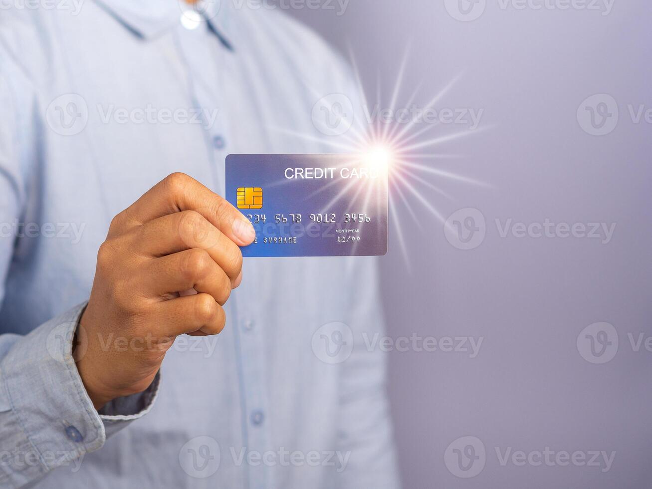 Midsection of a businessman wearing a light blue shirt holding a mockup blue credit card with star light effect while standing in a studio with copy space for text. Money and business concept photo