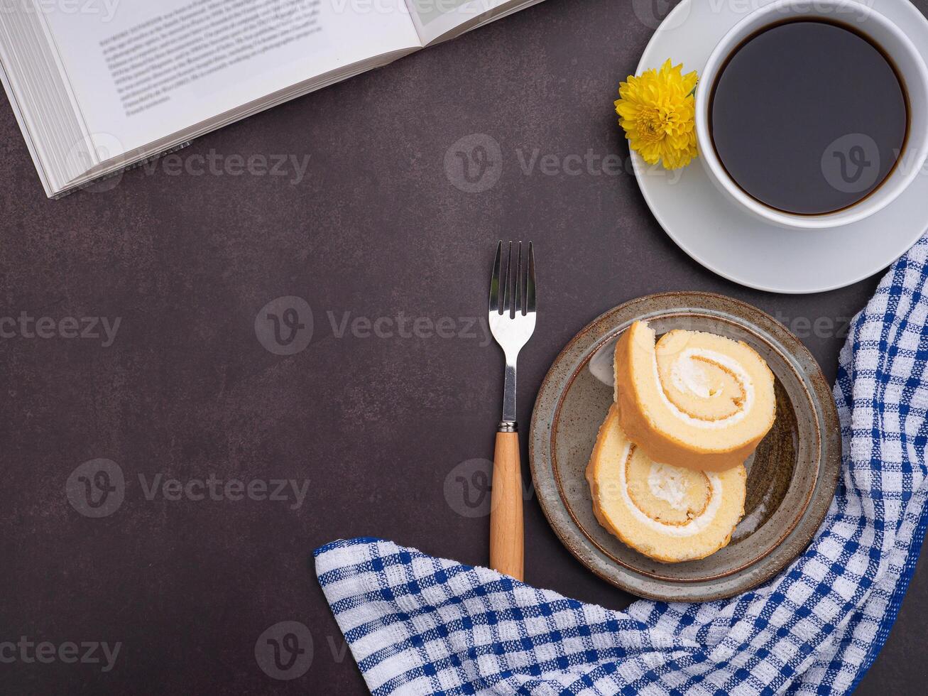 Top view of a book with roll cakes on a plate, a white coffee cup, and a cloth placed on dark gray stone background. Space for text. Concept of relaxation photo