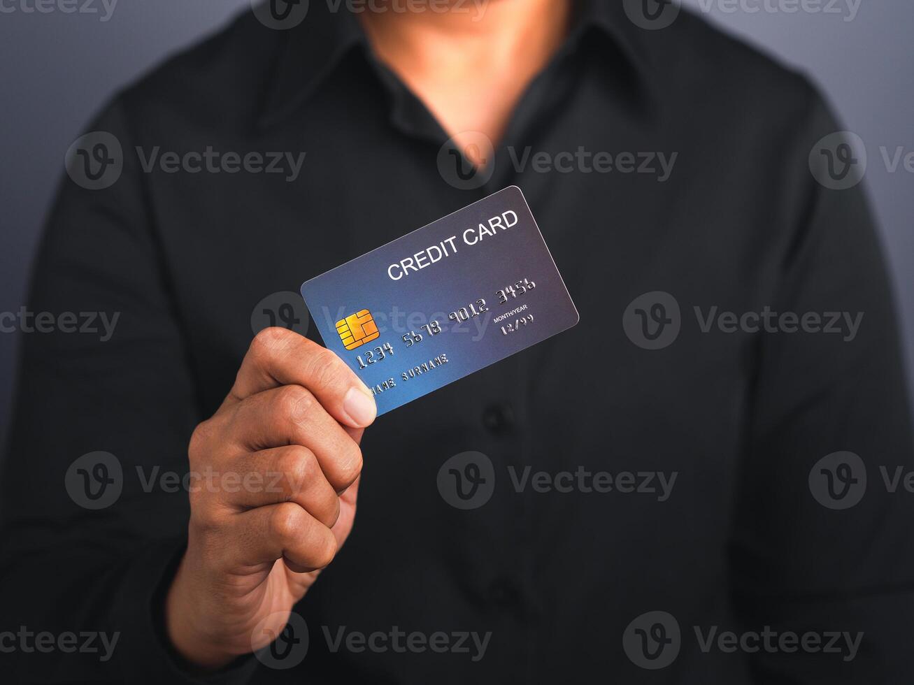 Businessman holding a mockup blue credit card while standing in a studio with copy space for text. Close-up photo. Money and business concept photo