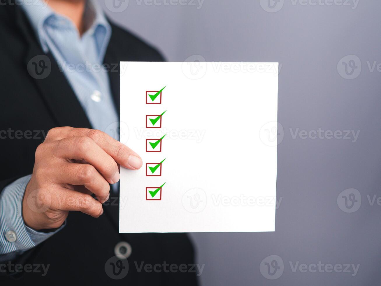 Midsection of a businessman holding a white paper with a checklist against a gray background photo