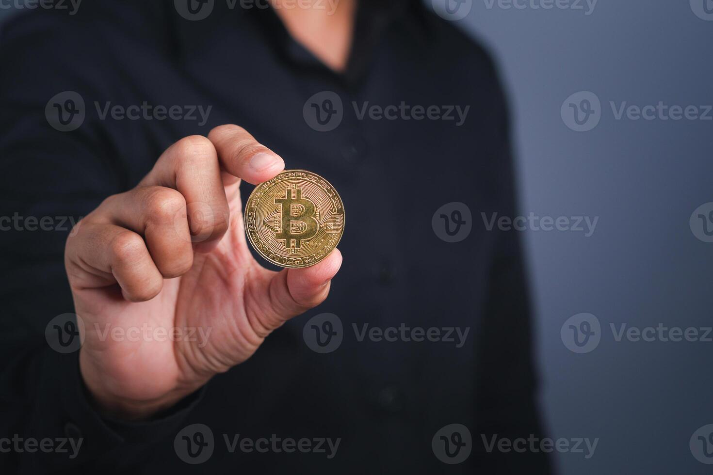 Investor guy showing a bitcoin golden coin with a dark gray background. Close-up photo. Space for text. Virtual cryptocurrency and future money concept photo