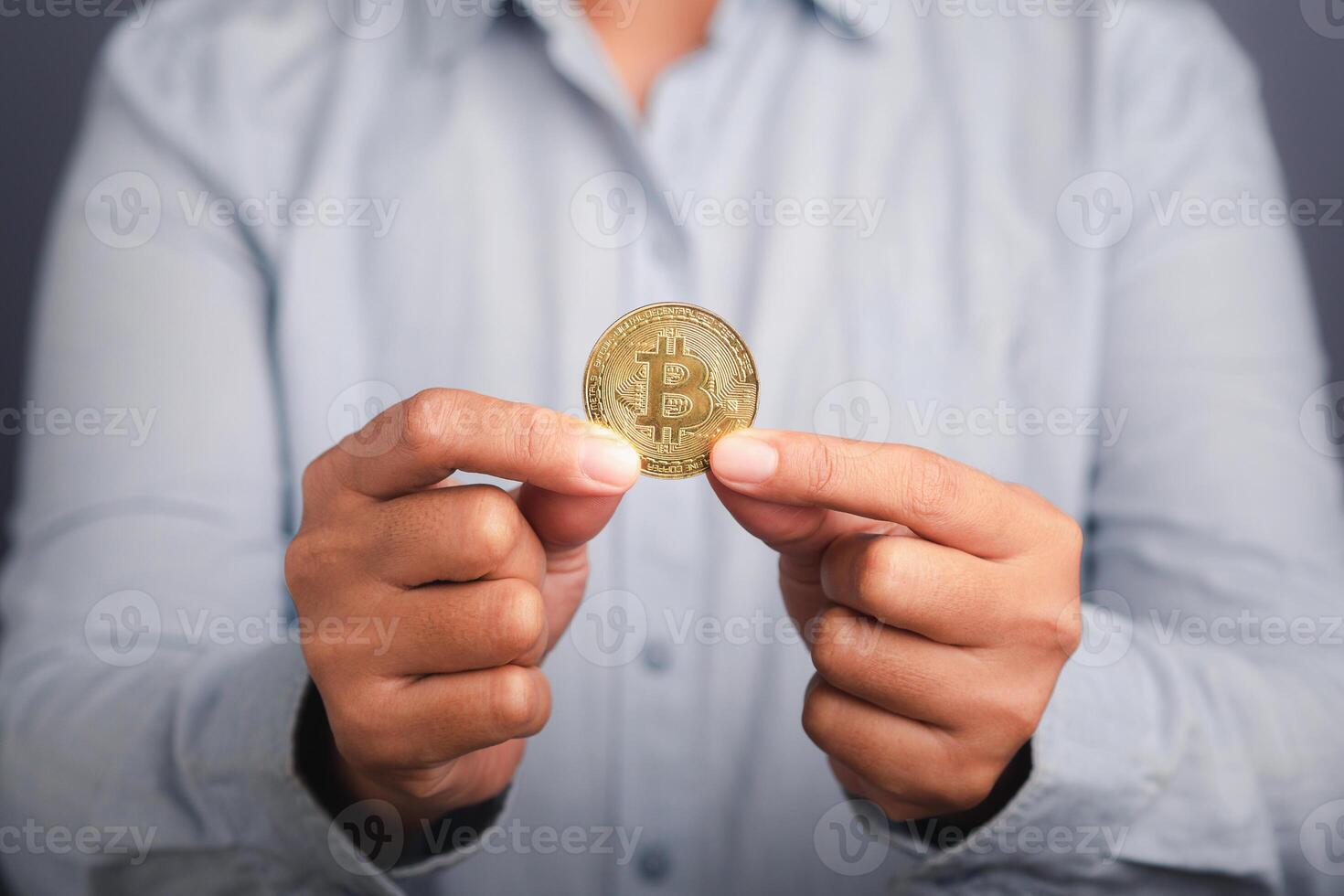 Investor guy showing a bitcoin golden coin with a gray background. Close-up photo. Space for text. Virtual cryptocurrency and future money concept photo