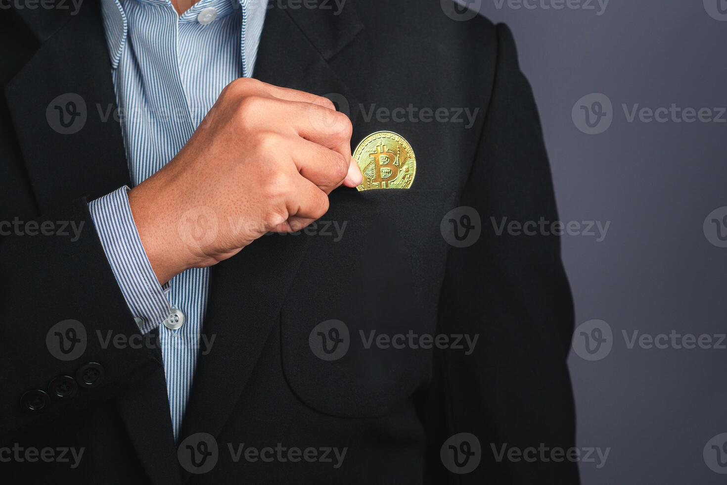 An investor guy holding a bitcoin golden coin put to suit pocket with a gray background. Close-up photo. Space for text. Virtual cryptocurrency and future money concept photo