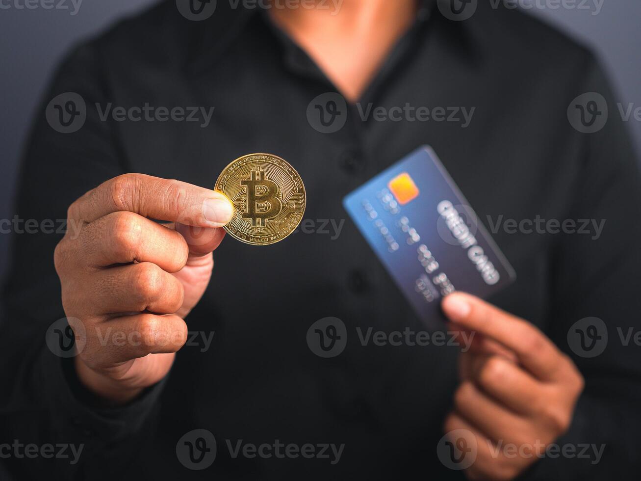 Investor guy showing a bitcoin golden coin and blue card while standing in the studio. Close-up photo. Space for text. Virtual cryptocurrency and future money concept photo