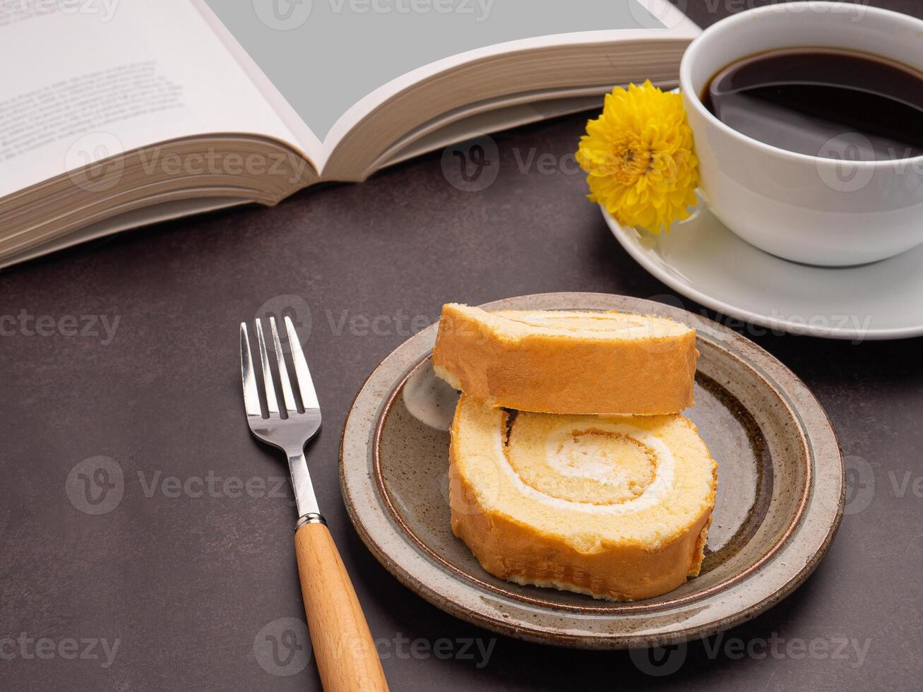 Top view of a book with roll cakes on a plate, a white coffee cup, and a cloth placed on a dark brown background. Space for text. Concept of reading and relaxation photo