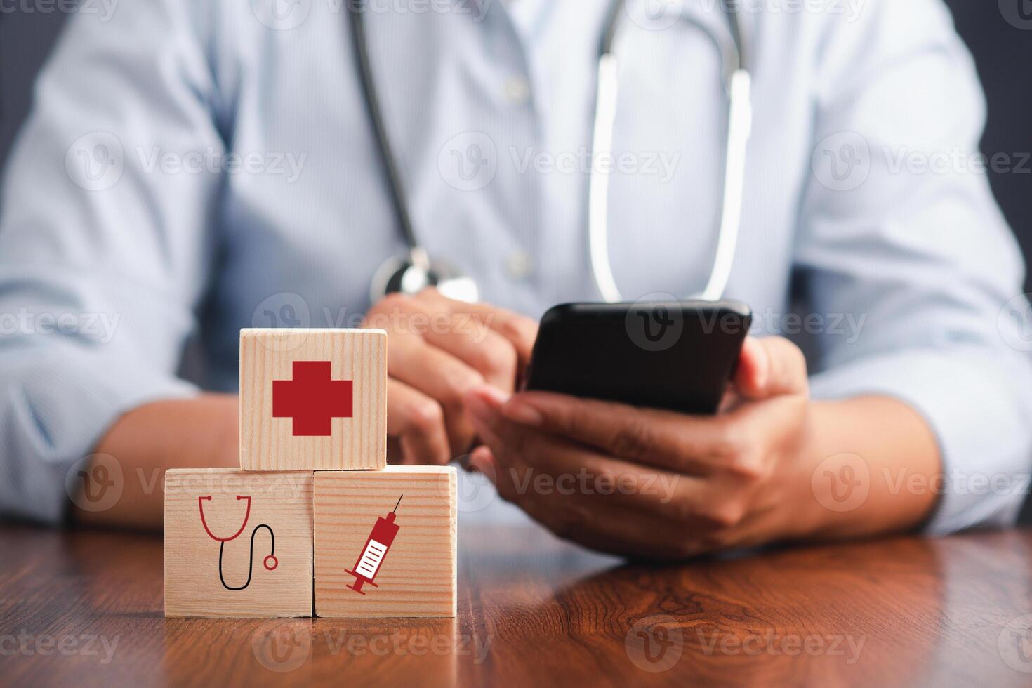 A doctor holding a smartphone and wooden blocks with icons of health and doctor while sitting on a chair. Close-up photo. Space for text. Concept of doctor and healthcare. photo