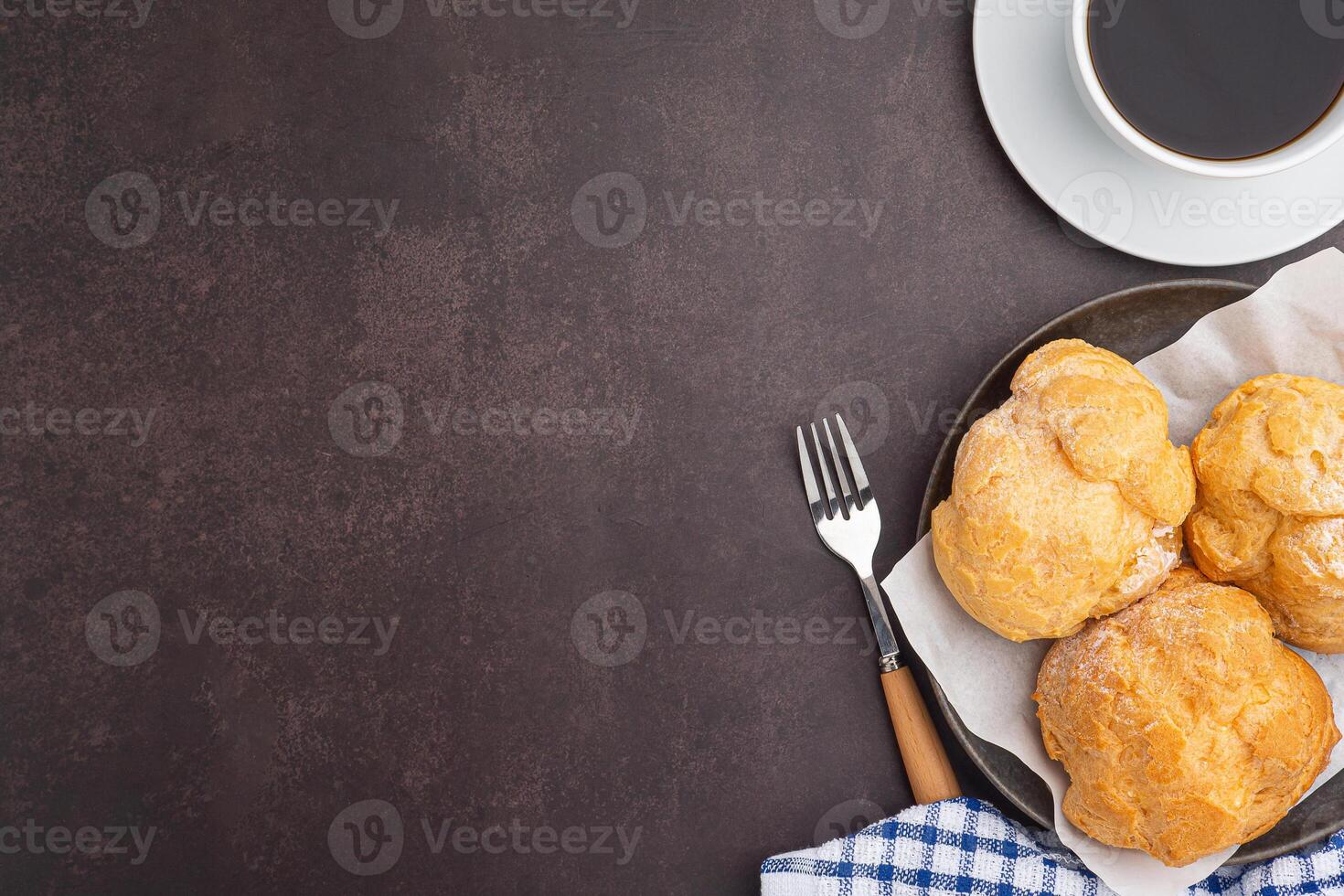 Top view of choux cream on a plate and a white coffee cup placed on a dark brown background. Space for text. Concept of relaxation photo