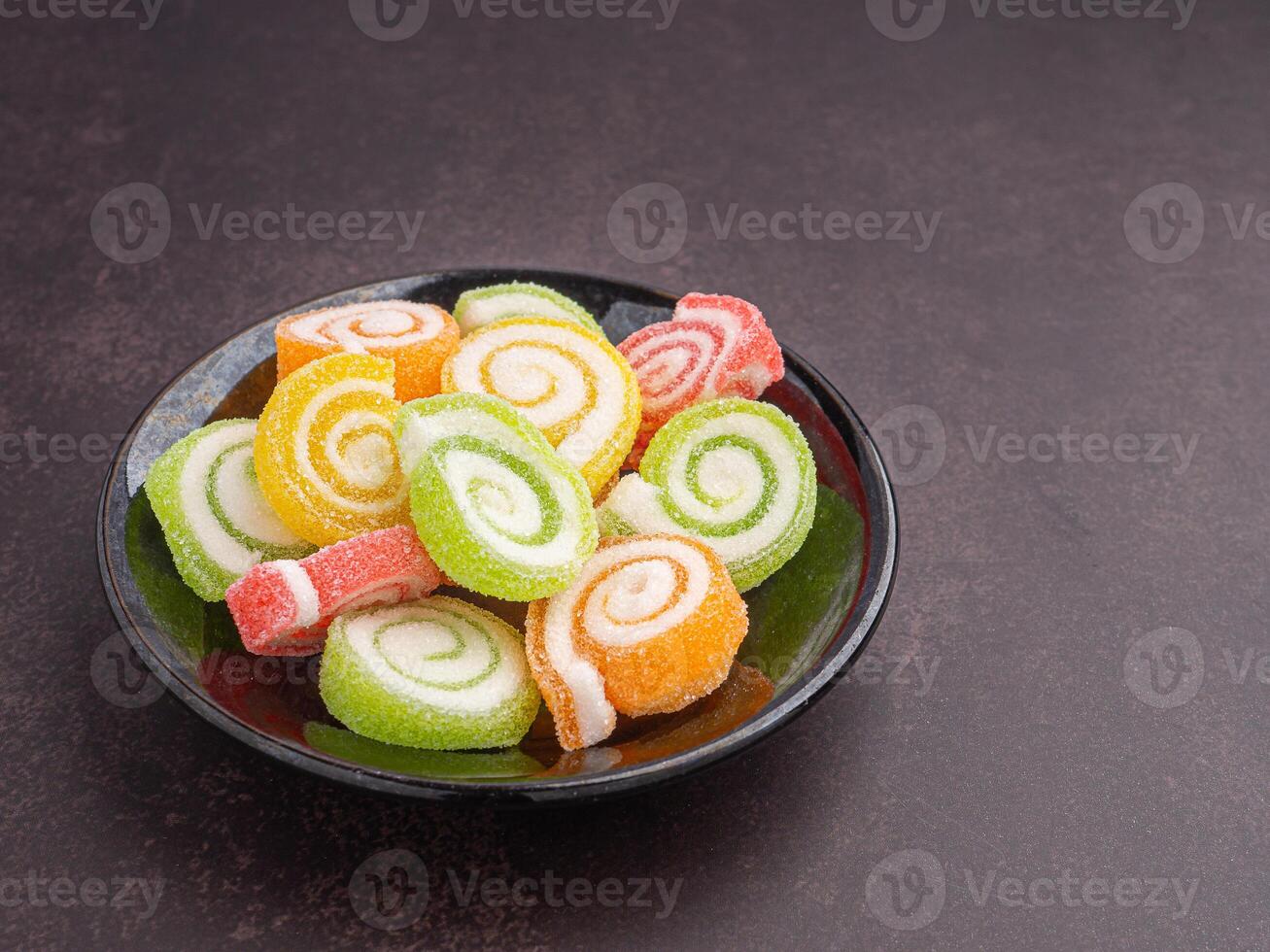 Colorful sweet jelly candy on a black plate with a book placed on dark brown background. Jelly circle breaded in sugar. Side view with copy space for text. Concept of dessert photo