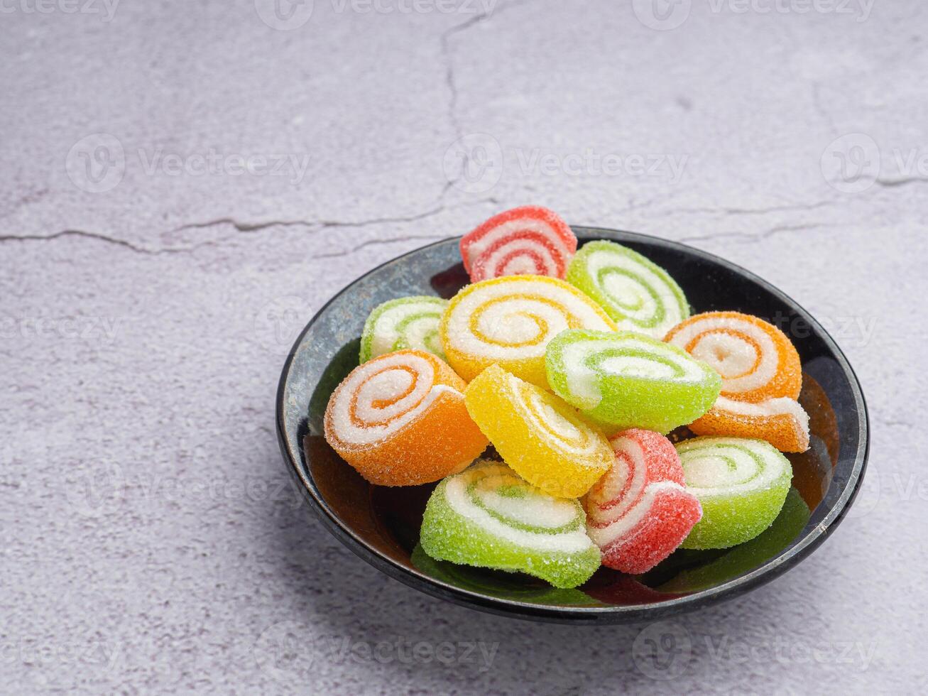 Colorful sweet jelly candy on a black plate with a book placed on gray stone background. Jelly circle breaded in sugar. Side view with copy space for text. Concept of dessert for children photo