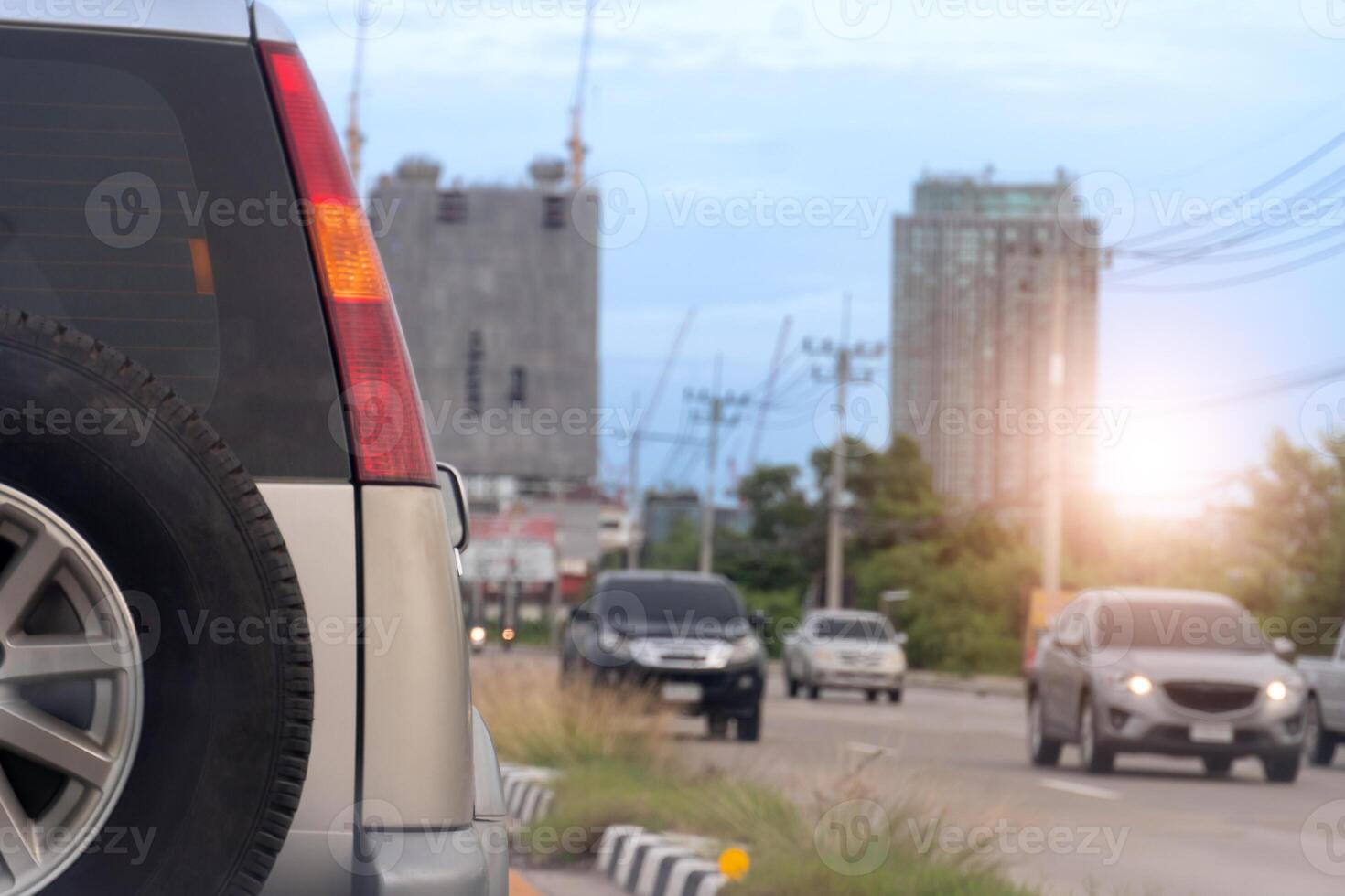 Rear side of traveling car on the road. The back has a spare tire attached. Many cars traveling rushed towards the opposite side. Background image with tall construction buildings in the city. photo