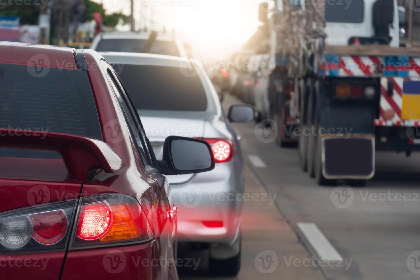 Rear side of red car on the road. Concrete road with many car during time on traffic jam. Speed light lines on the tail lights. Car parked in a long queue. photo