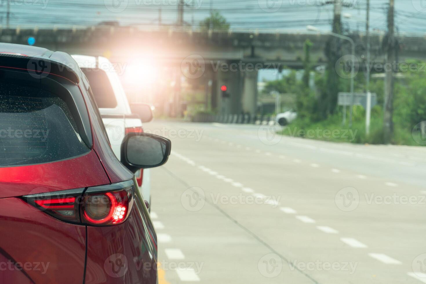 Luxury of red car stop on the road. Traveling in the provinces during the bright period. Open light brake. Concrete bridge crossing level intersection. and nature of green grass beside for background. photo