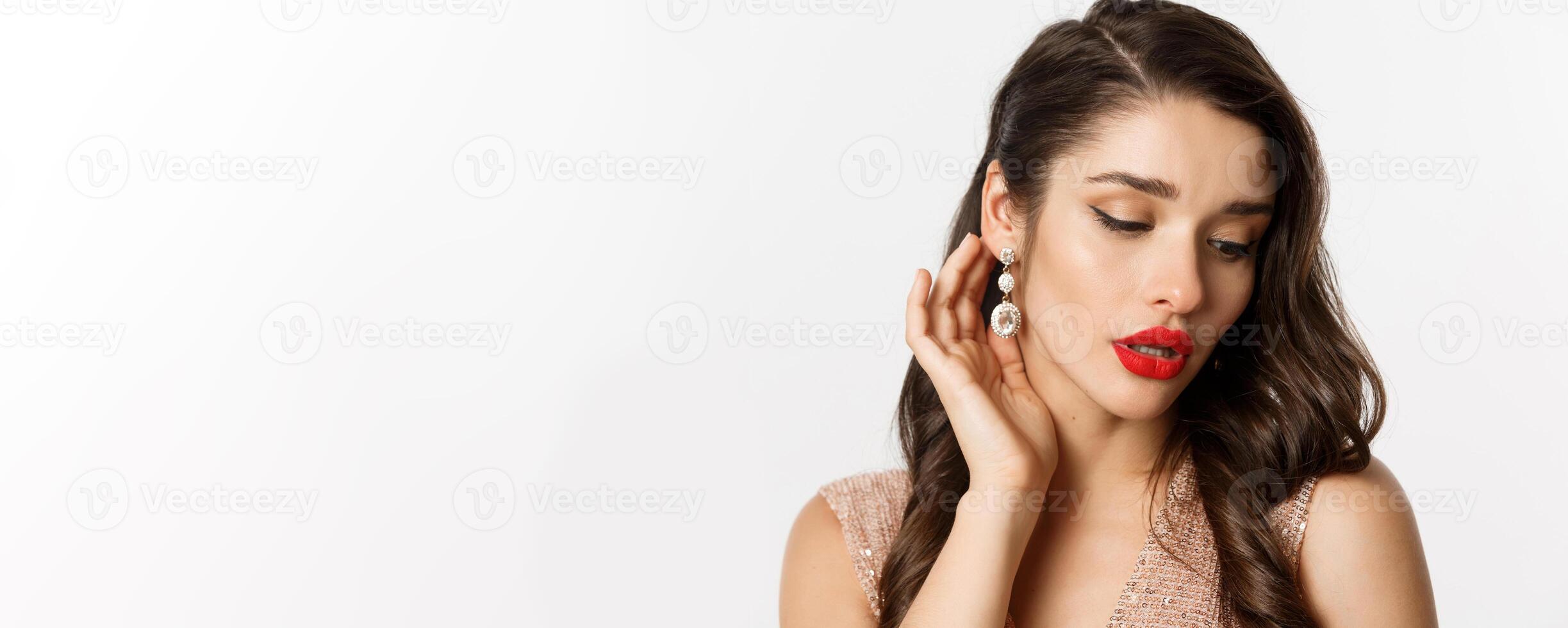 Concept of New Year celebration and winter holidays. Headshot of elegant brunette woman with red lips, showing earrings and looking sensual, white background photo