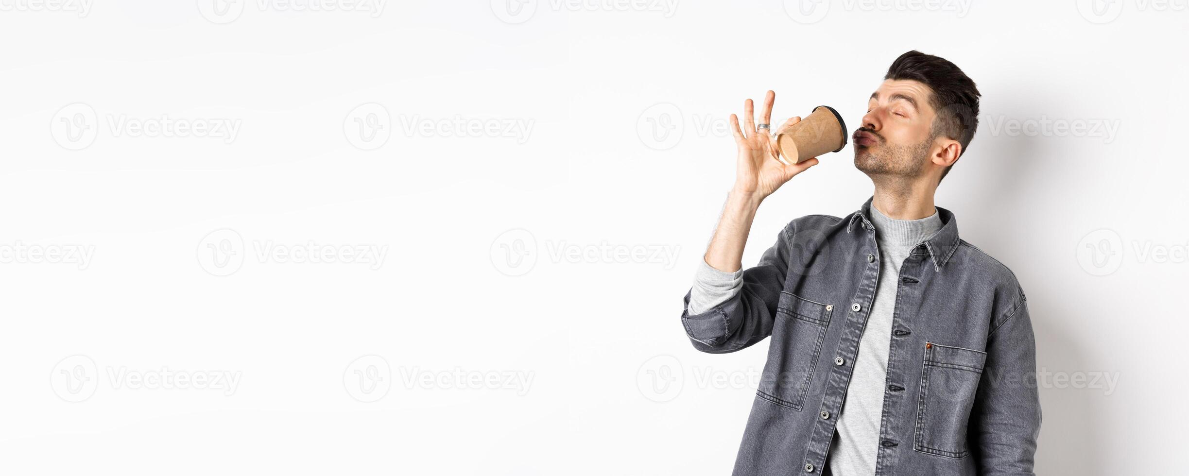 Funny guy enjoying drinking coffee from cup, sipping takeaway drink from cafe with satisfaction, standing on white background photo