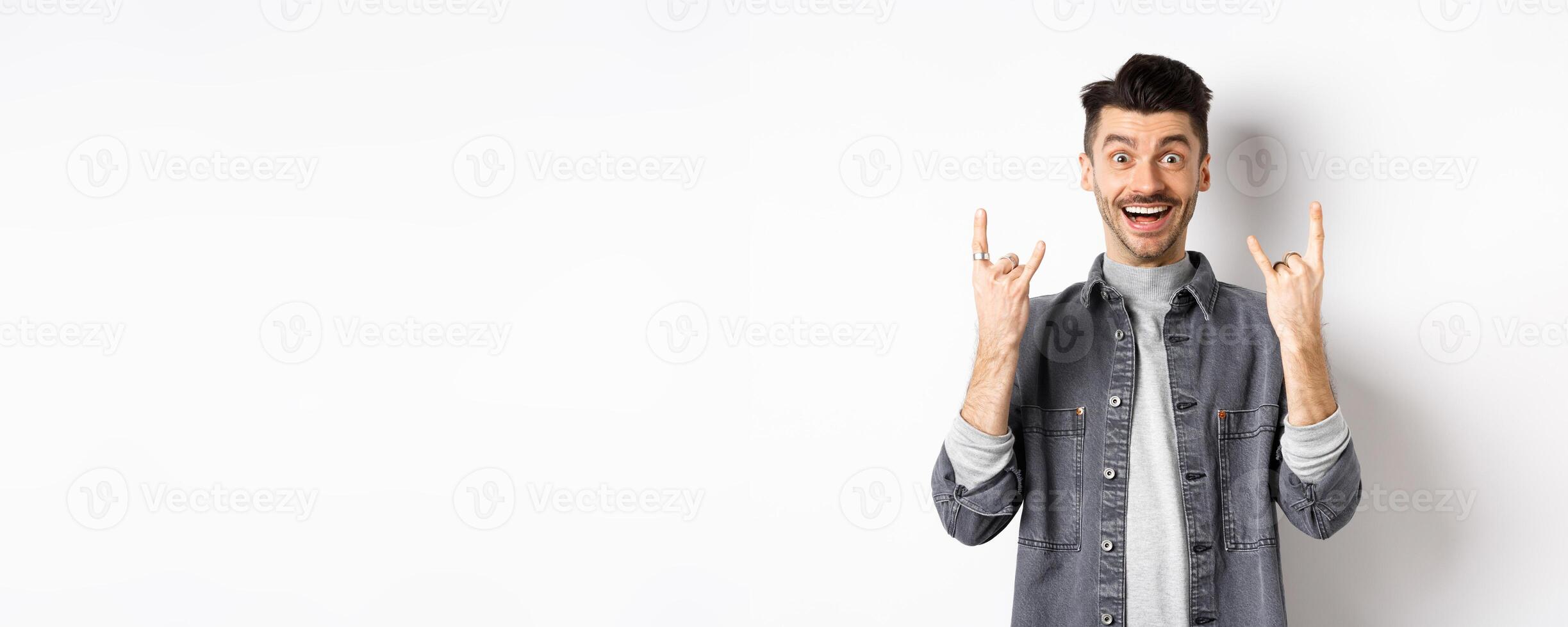 Happy and excited guy showing rock on gesture and having fun, enjoying event and smiling cheerful, standing on white background photo