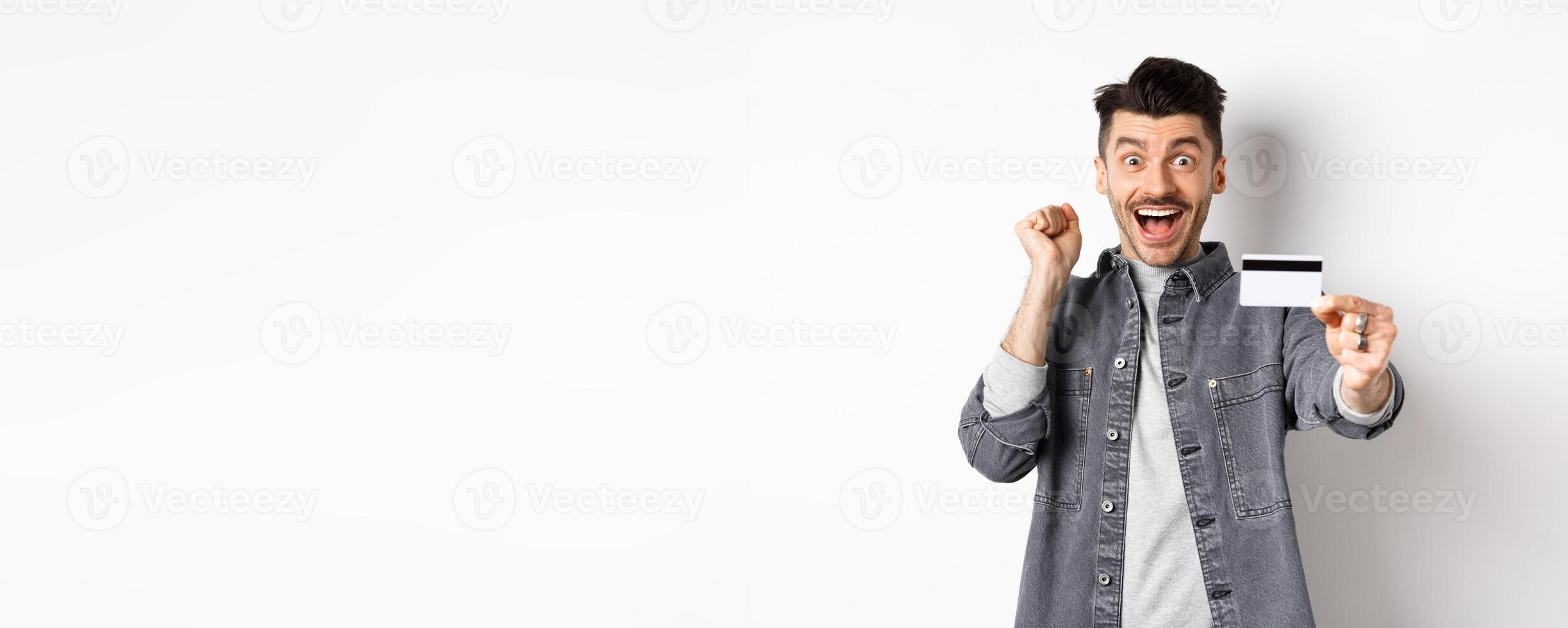 Happy man scream from excitement and show plastic credit card, recommending bank, standing on white background photo