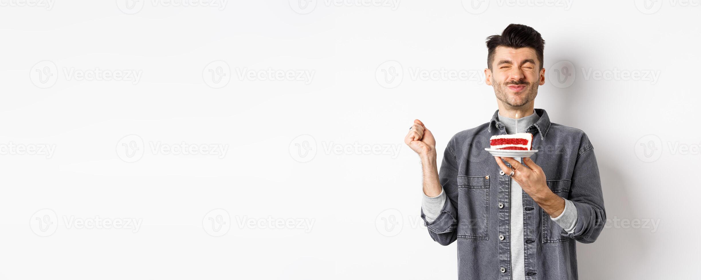 Happy birthday guy making wish on cake with candle, celebrating bday, standing on white background photo
