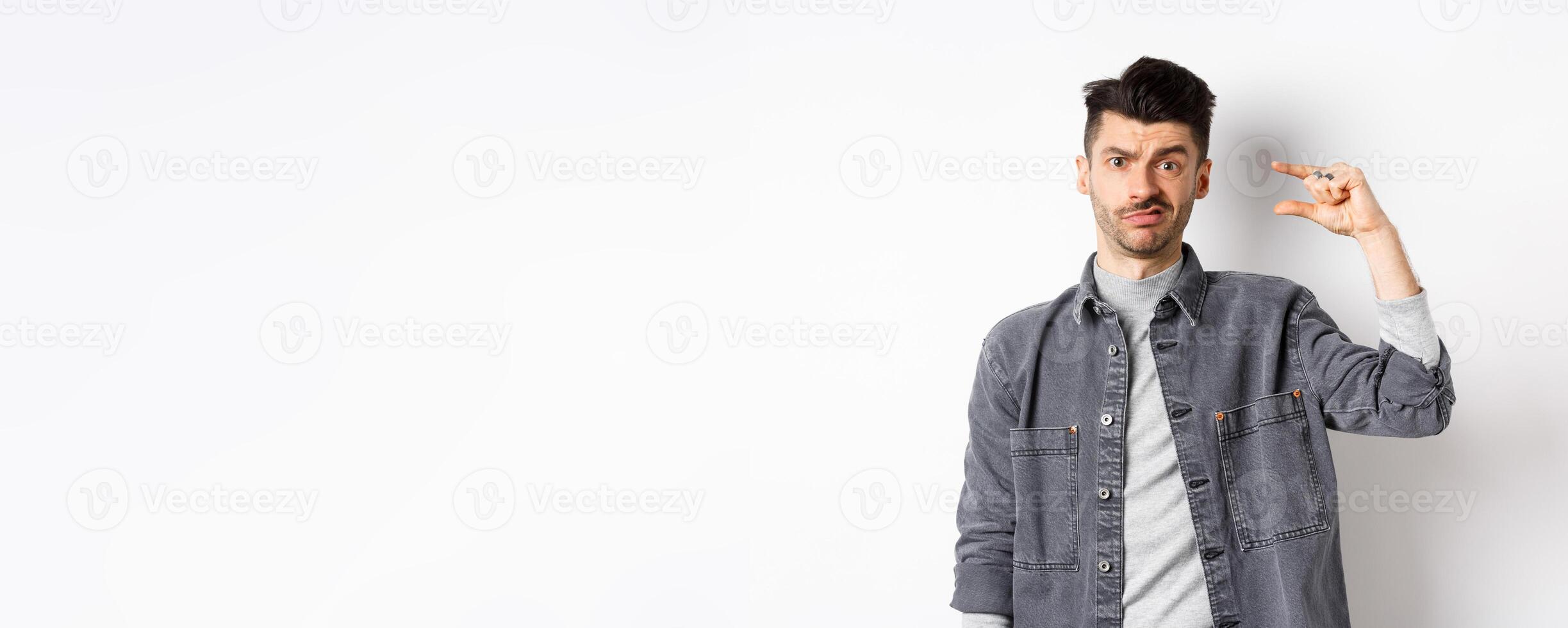 Disappointed guy showing small size and grimacing upset, frowning displeased with little thing, standing on white background photo