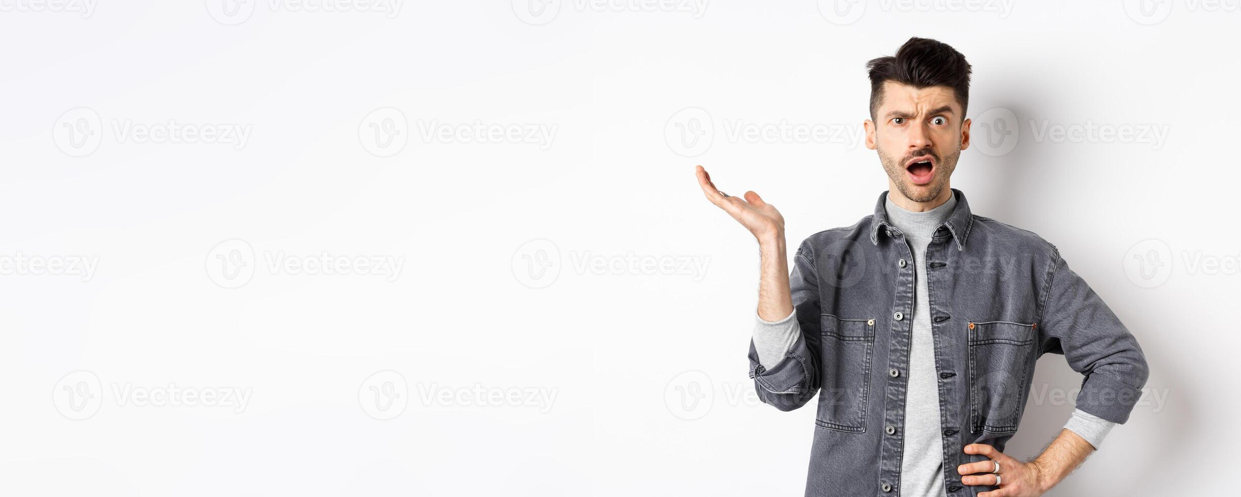 Confused and annoyed guy raising hand up and complaining, asking wtf happened, cant understand, standing on white background photo