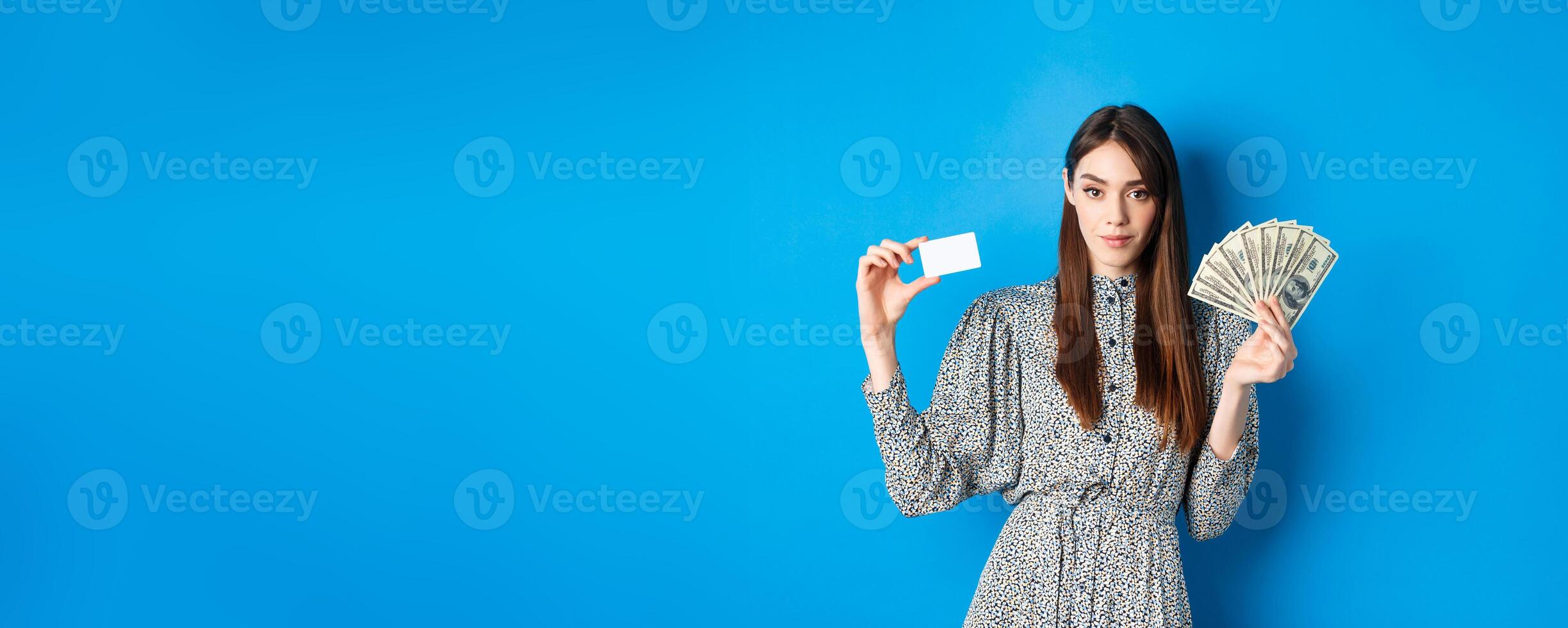 Shopping. Elegant sassy woman with dollar bills money and plastic credit card, looking confident at camera, blue background photo