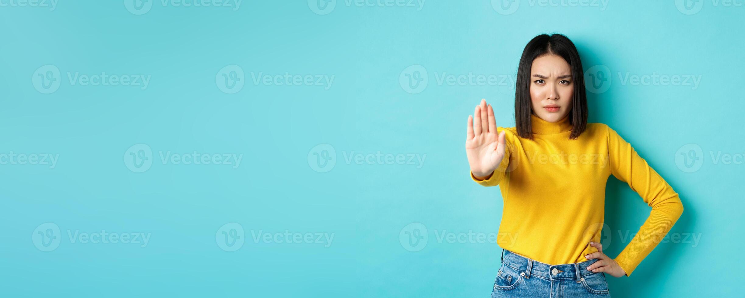 Confident and serious asian woman tell no, showing stop gesture to prohibit and warn, disagree with someone, standing upset against blue background photo