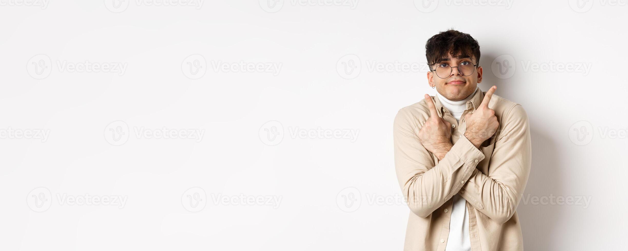Confused funny guy in glasses pointing fingers aside, showing two variants and look indecisive, cant choose, standing on white background photo